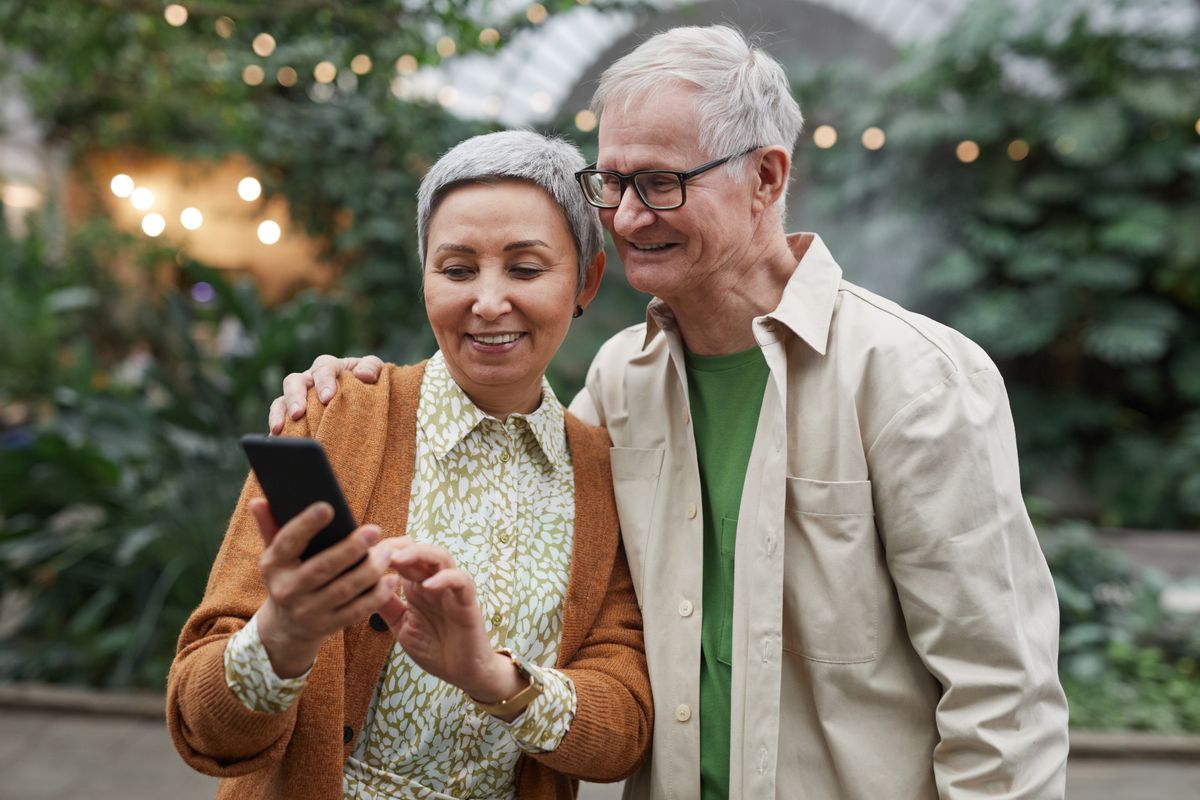 Coppia di anziani che sorride guardando insieme lo smartphone