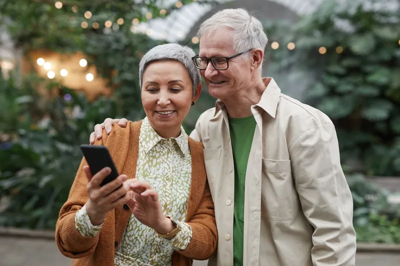 Coppia di anziani che sorride guardando insieme lo smartphone