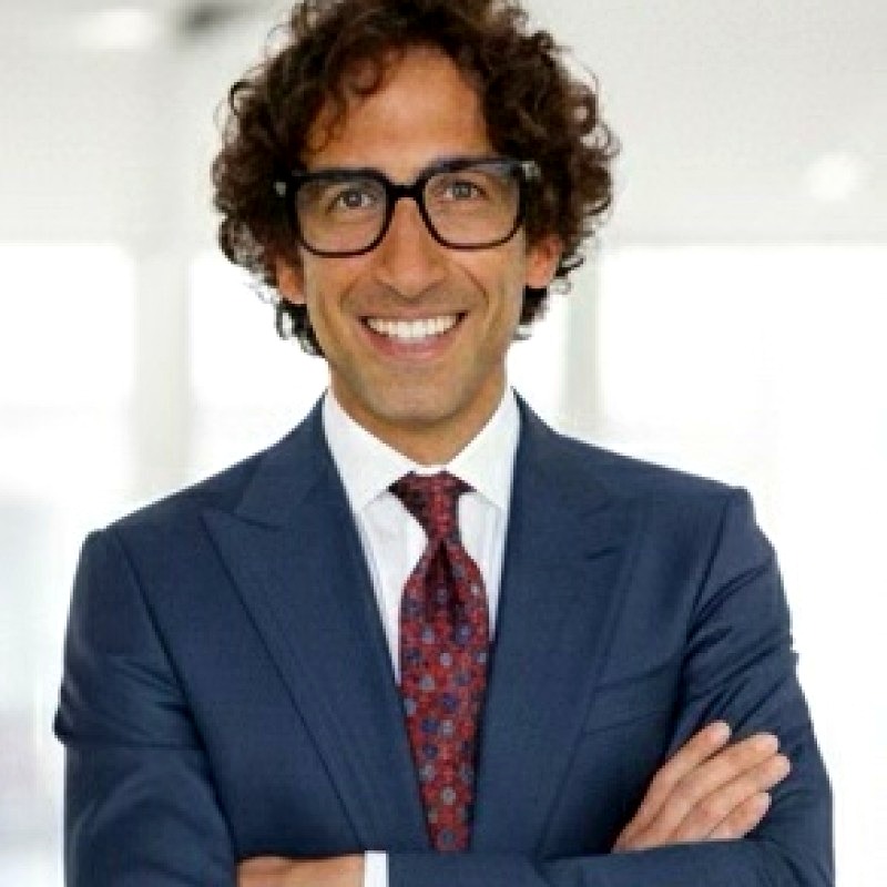 Ritratto in bianco e nero di Donato Marangelo, co-fondatore di MEMO: uomo sorridente con capelli ricci scuri, occhiali dalla montatura nera, giacca e cravatta, braccia conserte