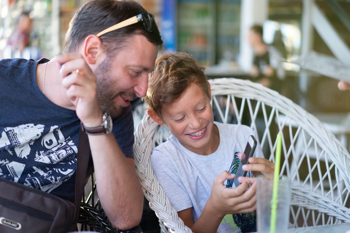 Padre e figlio adolescente che ridono guardando insieme lo smartphone