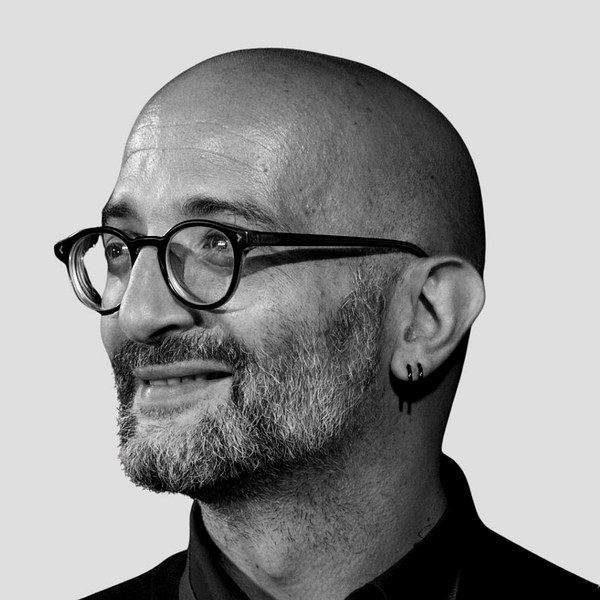 Ritratto in bianco e nero di Giovanni Bibbò, co-fondatore tecnico di MEMO: uomo calvo con occhiali tondi e barba corta, sorridente di profilo